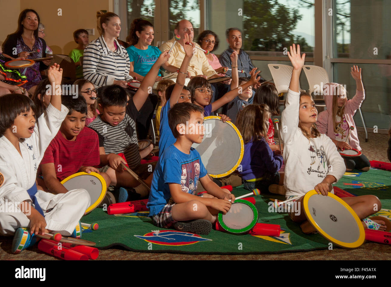 Halten Sie kleine Trommeln, express gemischtrassigen Kinder ihre Begeisterung für das Spielen in einer Rhythmus-Band bei einem Laguna Niguel, CA, Stadtbibliothek Mehrzweckraum. Beachten Sie die Eltern im Hintergrund. Stockfoto