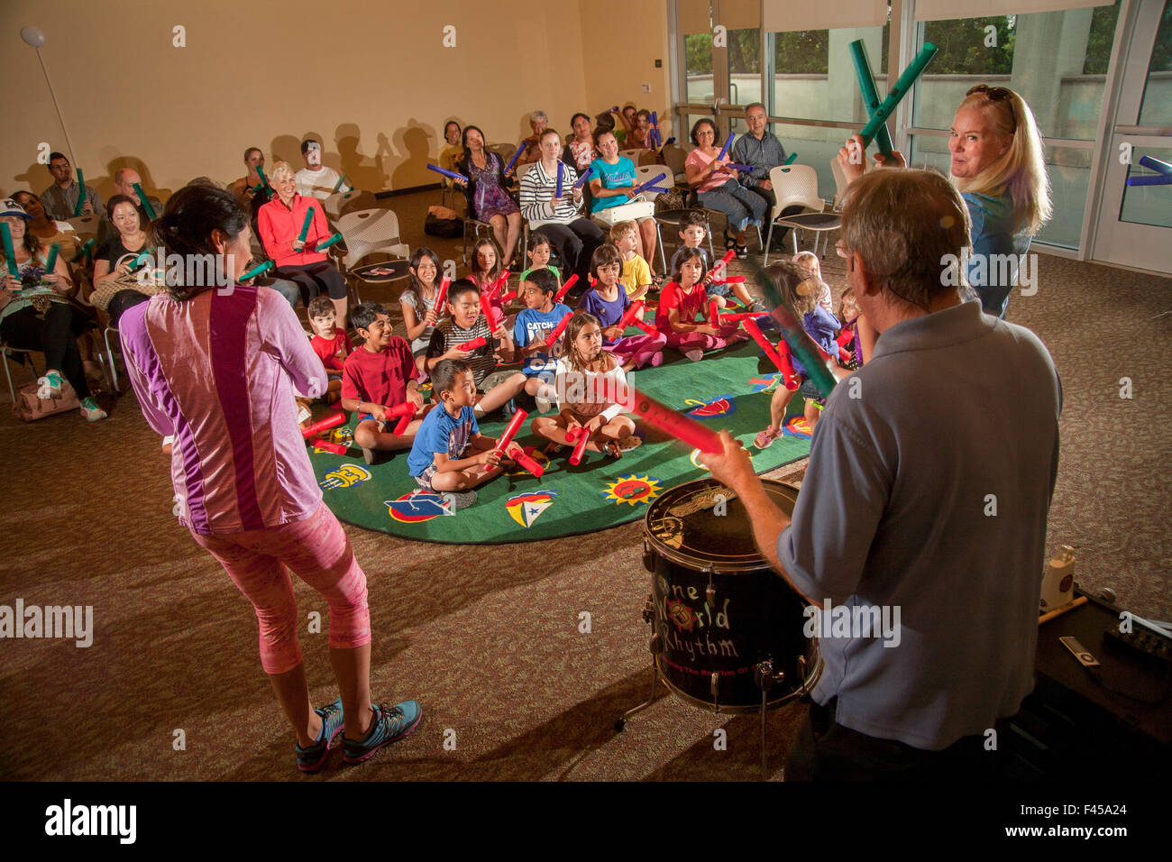 Eine multirassische Kinder Rhythm Band spielt tuned Percussion Röhren Boomwhackers am Laguna Niguel, CA, Stadtbibliothek Mehrzweckraum aufgerufen. Beachten Sie die Eltern im Hintergrund. Hinweis Erwachsenen Marktführer im Vordergrund Stockfoto