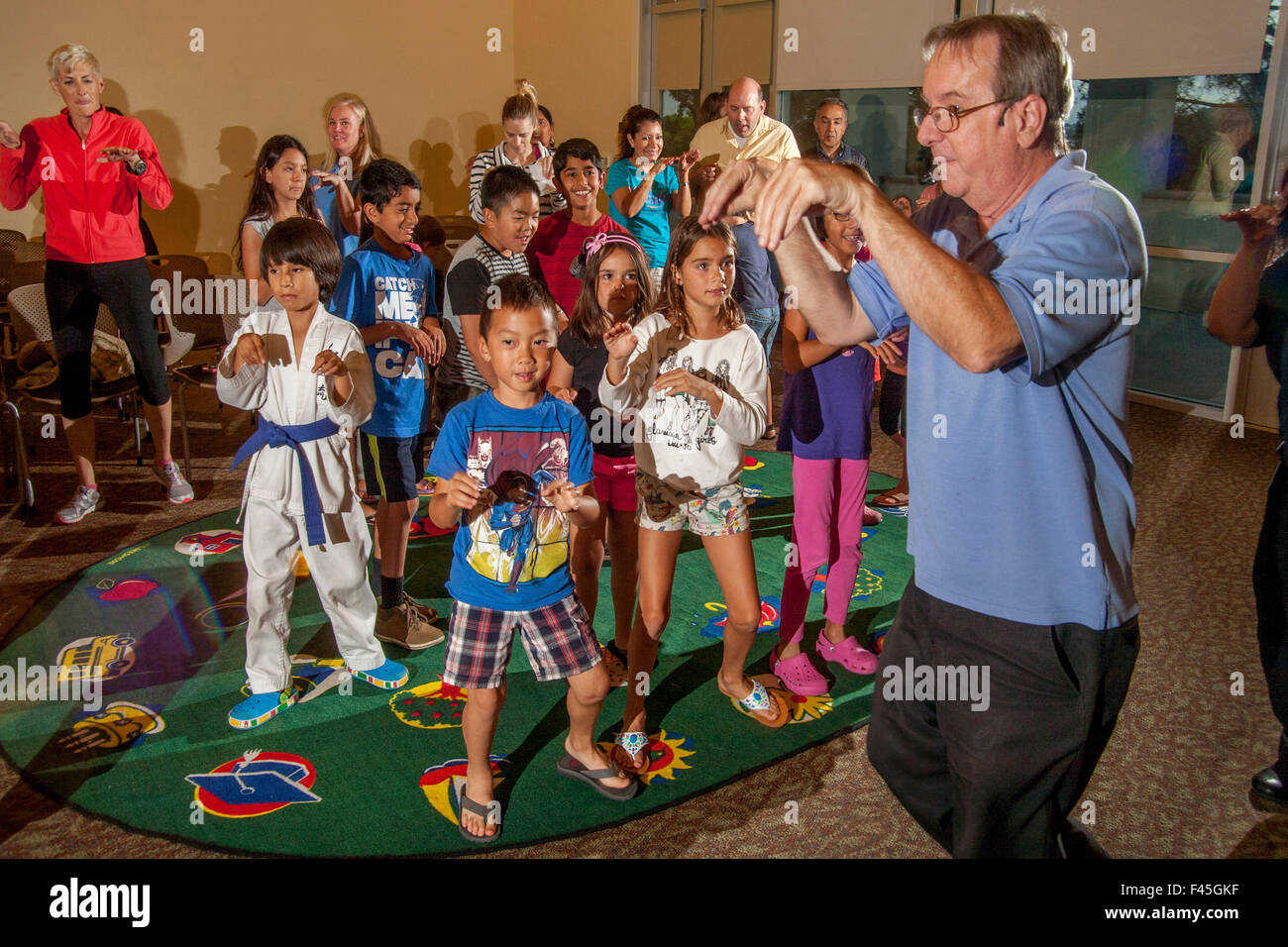 Laguna Niguel, CA, Musiker führt Kinder in einem amüsanten Zombie-Tanz bei einem Rhythmus-Band-Konzert in der örtlichen Bibliothek Mehrzweckraum. Stockfoto