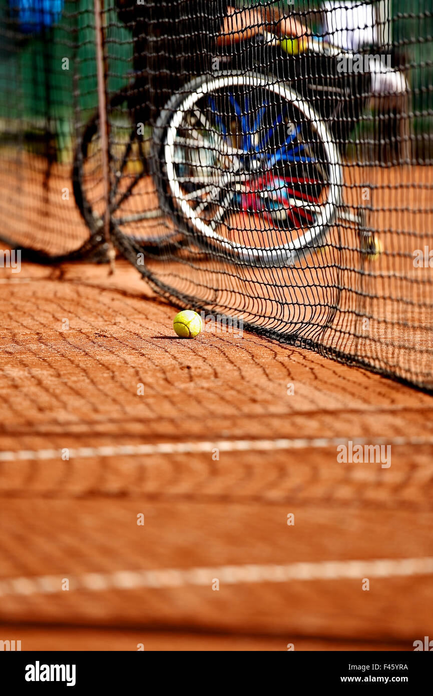 Unkonzentriert Rollstuhl-Tennis-Spieler ist hinter einer Tennis net auf einem Sandplatz gesehen. Stockfoto