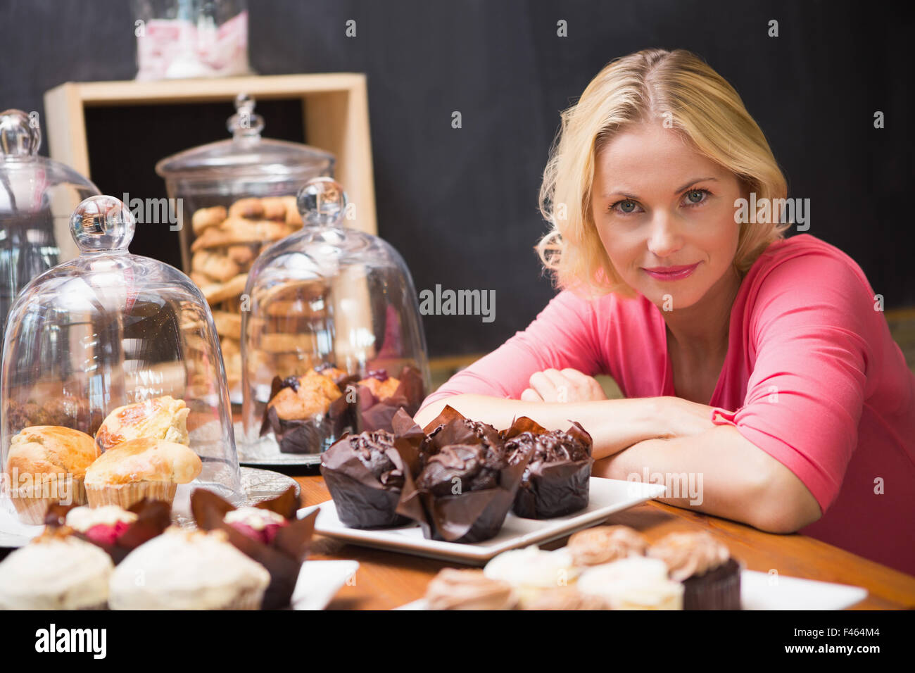 Hübsche Blondine lächelt in die Kamera neben Kuchen Stockfoto