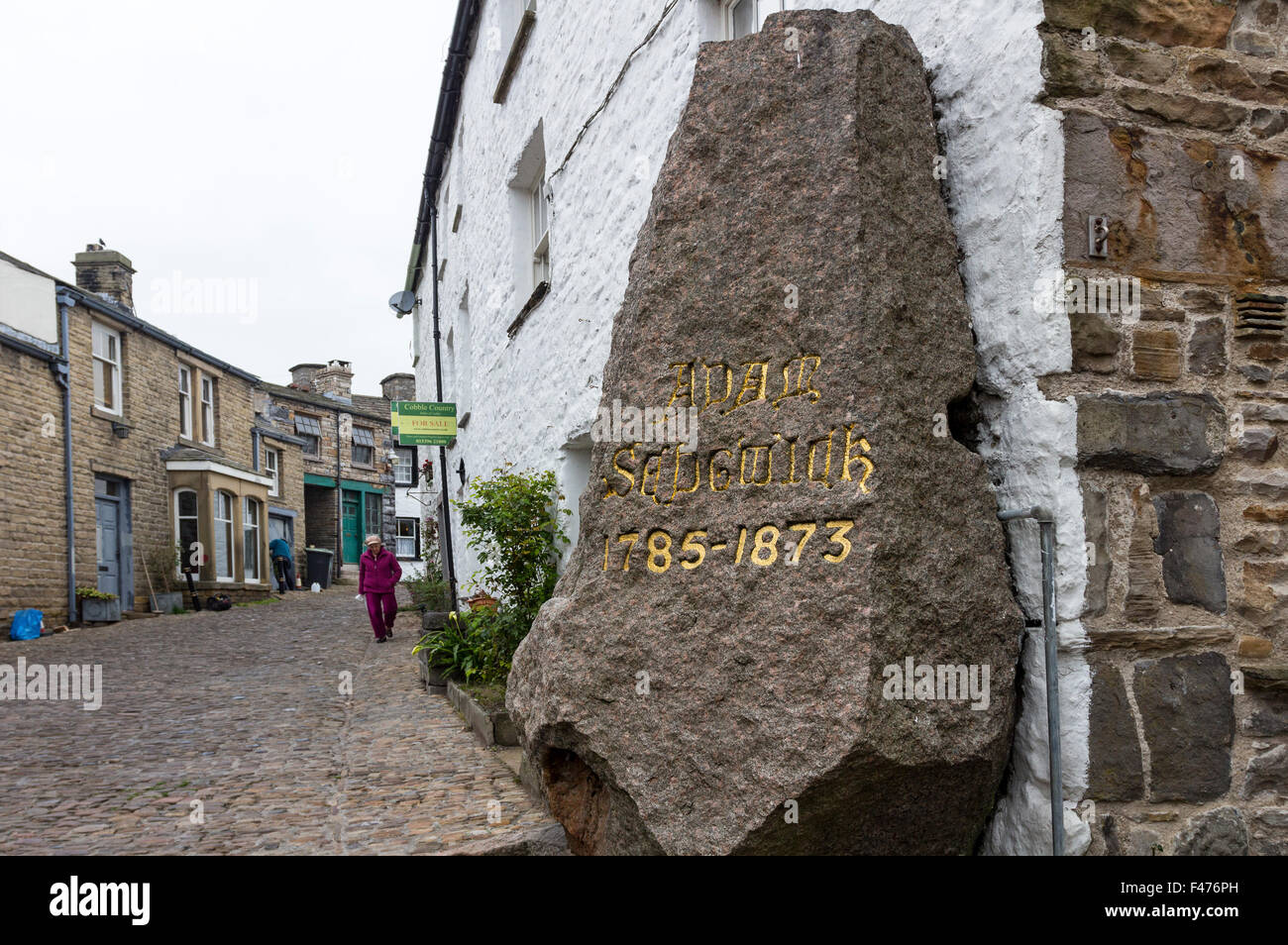 Granitdenkmal für Geologen Adam Sedgwick mit Haus für Verkauf Zeichen hinter im Dorf Dent, Dentdale, Cumbria UK Stockfoto