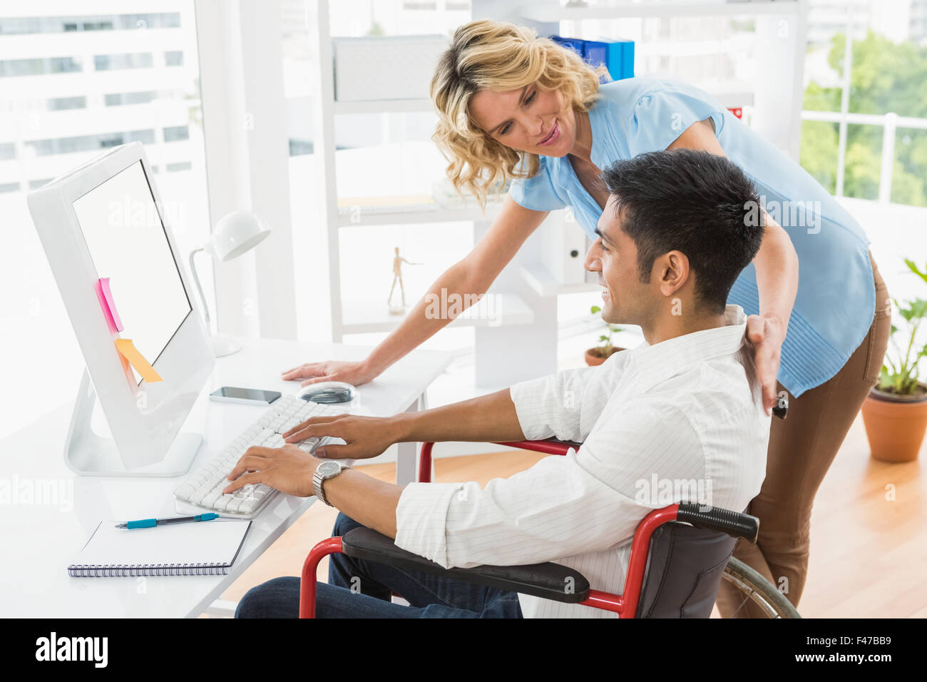 Lächelnde Jungunternehmer in einem Rollstuhl, Hilfe von einer Geschäftsfrau Stockfoto