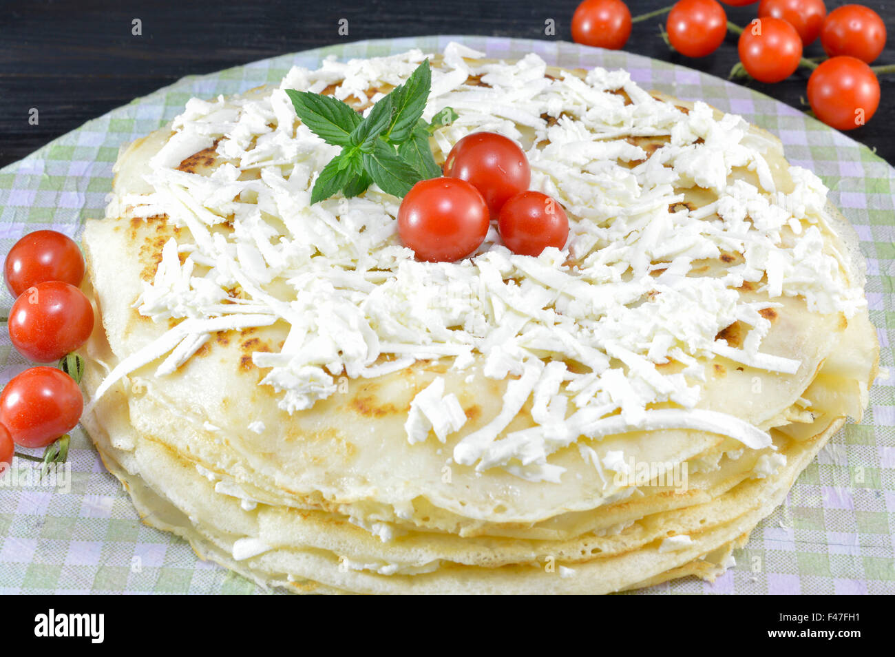 Hausgemachte Pfannkuchen auf dem Teller gestapelt und bedeckt mit Cherry-Tomaten und Käse Stockfoto