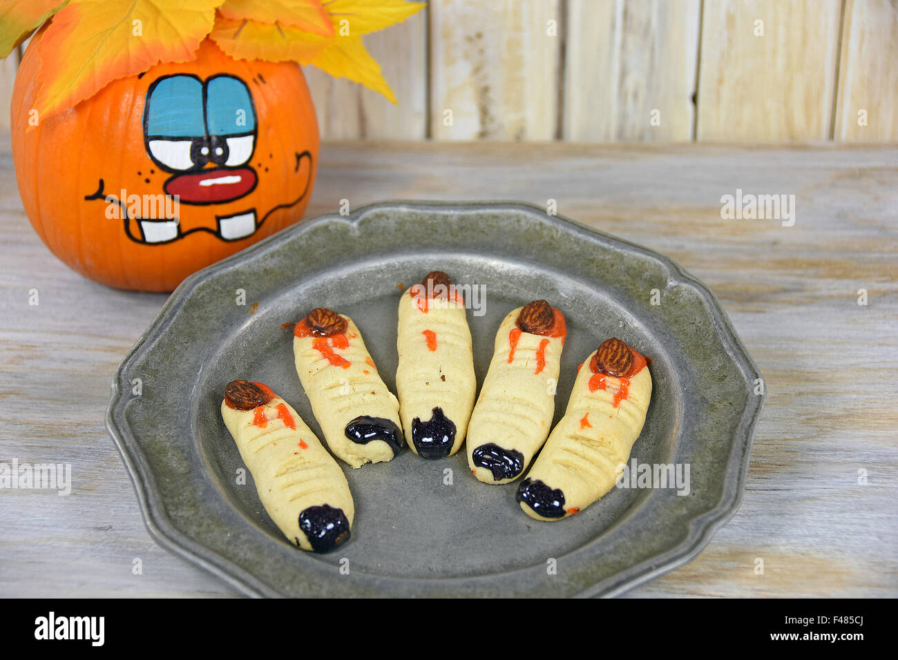 Halloween-Finger-Plätzchen mit lustigen Gesicht gemalt auf Herbst Kürbis. Stockfoto