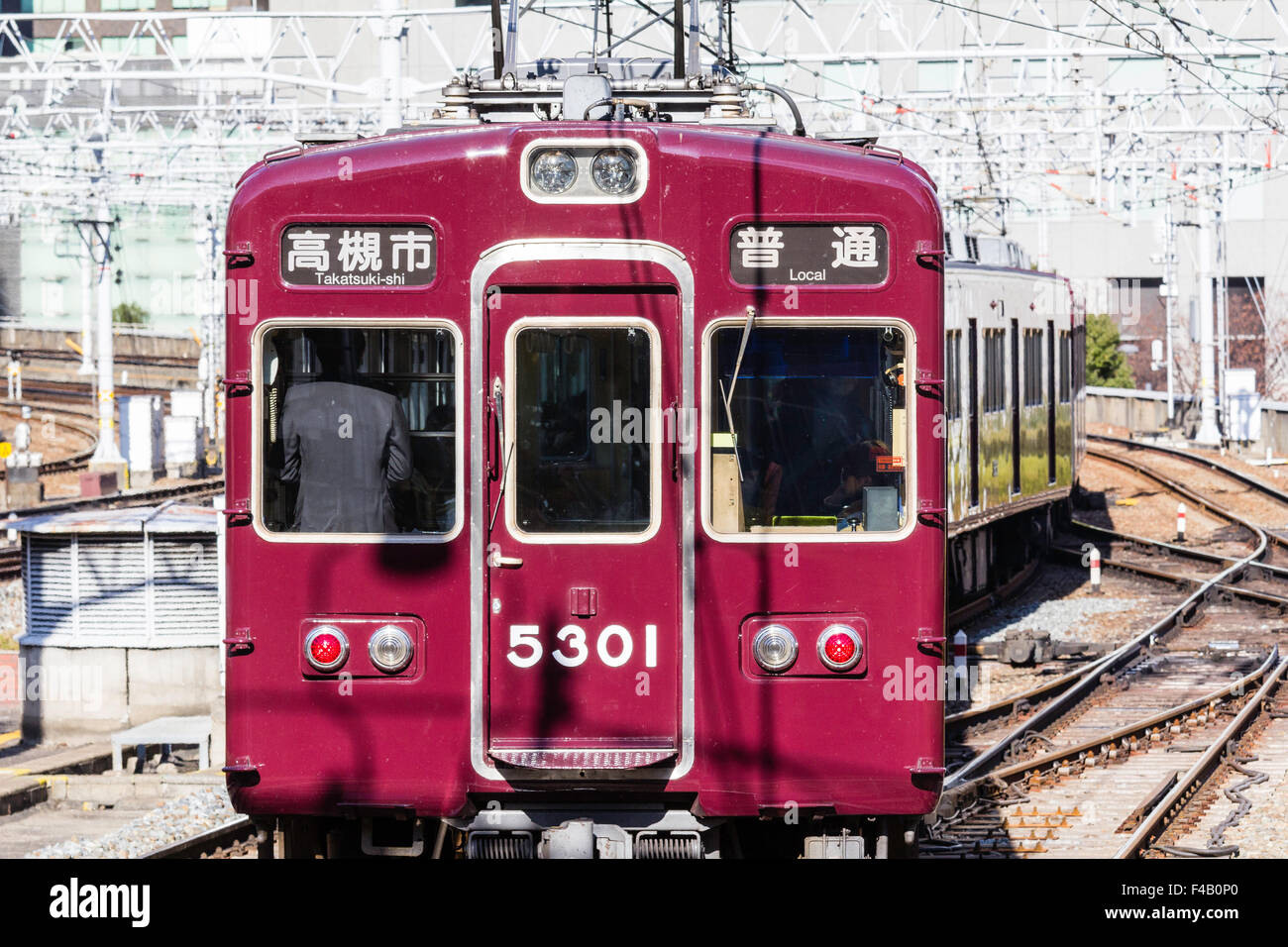Japan, Osaka Umeda. Private Hankyu Eisenbahn, kastanienbraun gefärbt Zug in Richtung Betrachter auf Titel mit obenliegenden elektrischen Drähten. Stockfoto