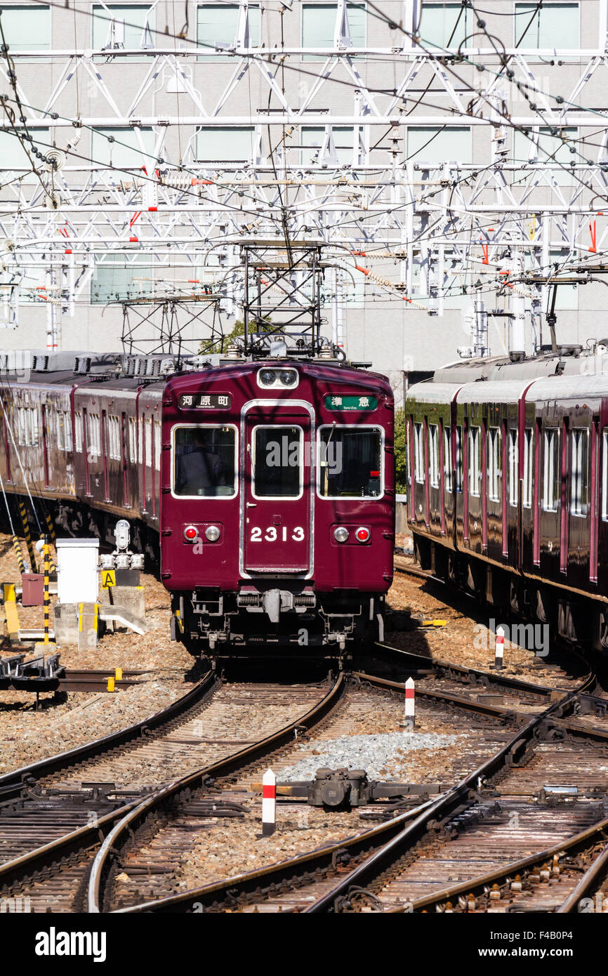 Japan, Osaka Umeda. Private Hankyu Eisenbahn, kastanienbraun gefärbt semi Express Zug in Richtung Betrachter auf Titel mit obenliegenden elektrischen Drähten. Stockfoto