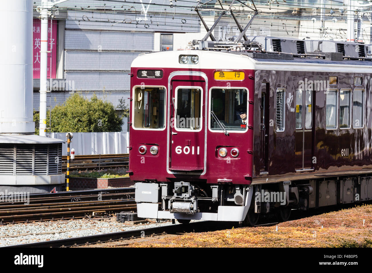 Japan, Osaka Umeda. Private Hankyu Eisenbahn, kastanienbraun gefärbt Express Zug in Richtung Betrachter auf Titel mit obenliegenden elektrischen Drähten. Stockfoto