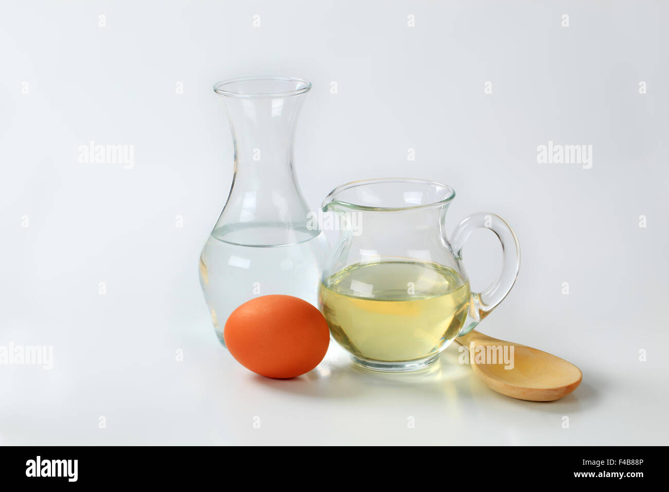 Karaffe mit kaltem Wasser, Krug mit Sonnenblumenöl, Ei und Löffel aus Holz Stockfoto