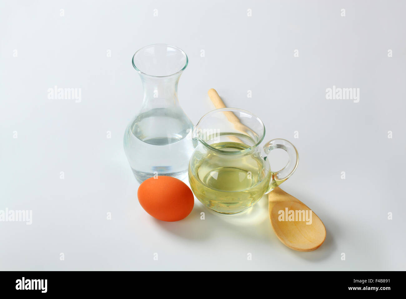 Karaffe mit kaltem Wasser, Krug mit Sonnenblumenöl, Ei und Löffel aus Holz Stockfoto
