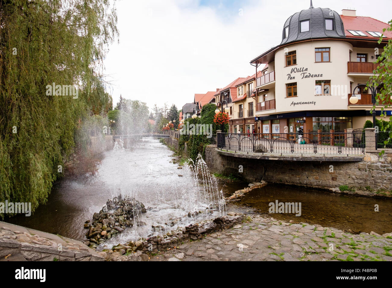 Wasser-Brunnen am Bystrzyca Dusznicka River mit Geschäften im Zentrum des Kurorts Piemont. Polanica-Zdrój, Niederschlesien, Polen Stockfoto