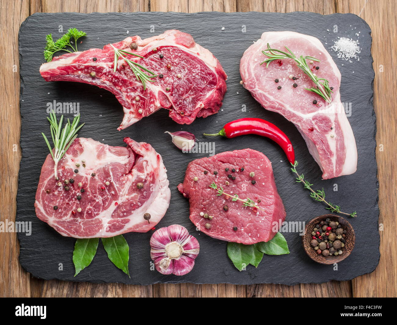 Rohes Fleisch Steaks mit Gewürzen auf dem schwarzen Schneidebrett. Stockfoto