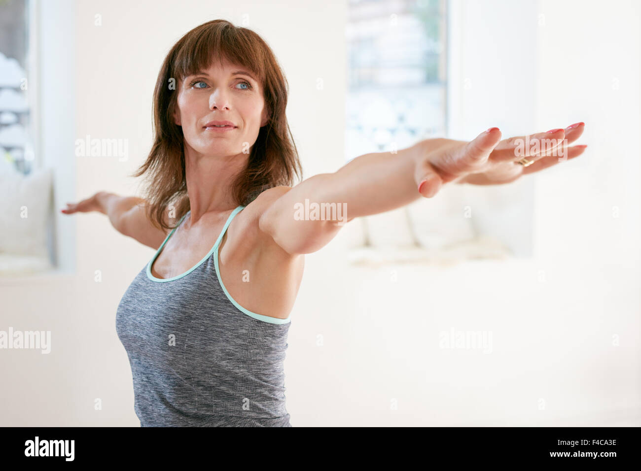 Porträt von Reife Frau streckte ihre Arme und wegschauen im Fitnessstudio. Schöne Frau darstellende Yoga in Krieger darstellen, Virabhadr Stockfoto