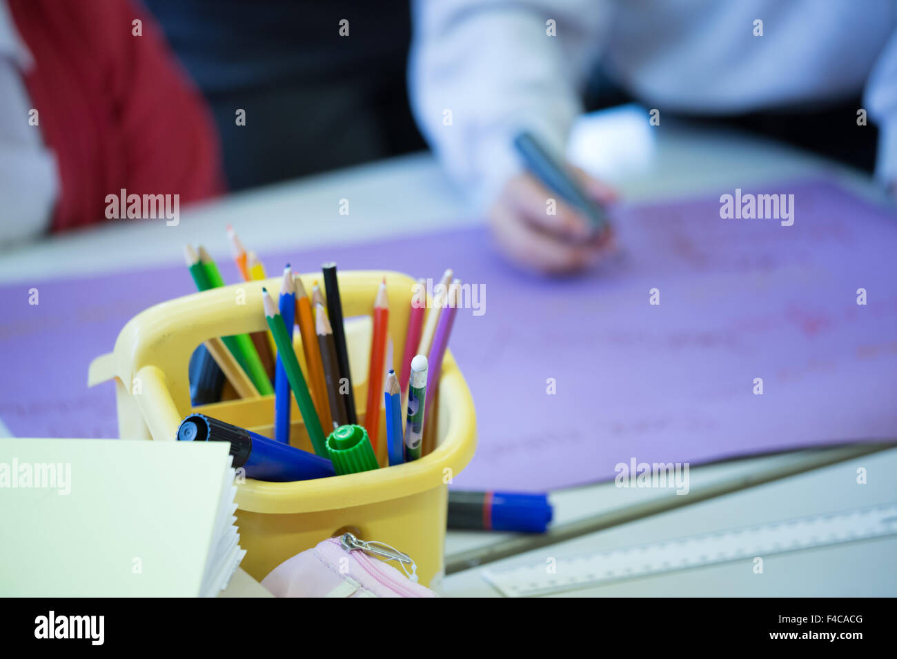 Ein typisches UK Grundschule Klassenzimmer mit Farbstiften im Vordergrund und Schülern im Hintergrund Stockfoto