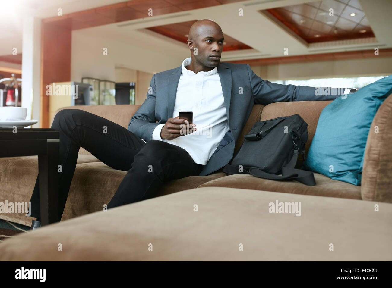 Schuss von afrikanischen Geschäftsmann mit einem Handy in der hand, sitzt auf der Couch wegsehen. Junger Geschäftsmann warten im hote Stockfoto