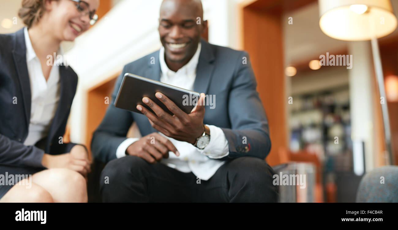 Glückliche junge Geschäftsleute sitzen zusammen mit digital-Tablette in der Hotellobby. Tablet-Computer im Mittelpunkt. Stockfoto