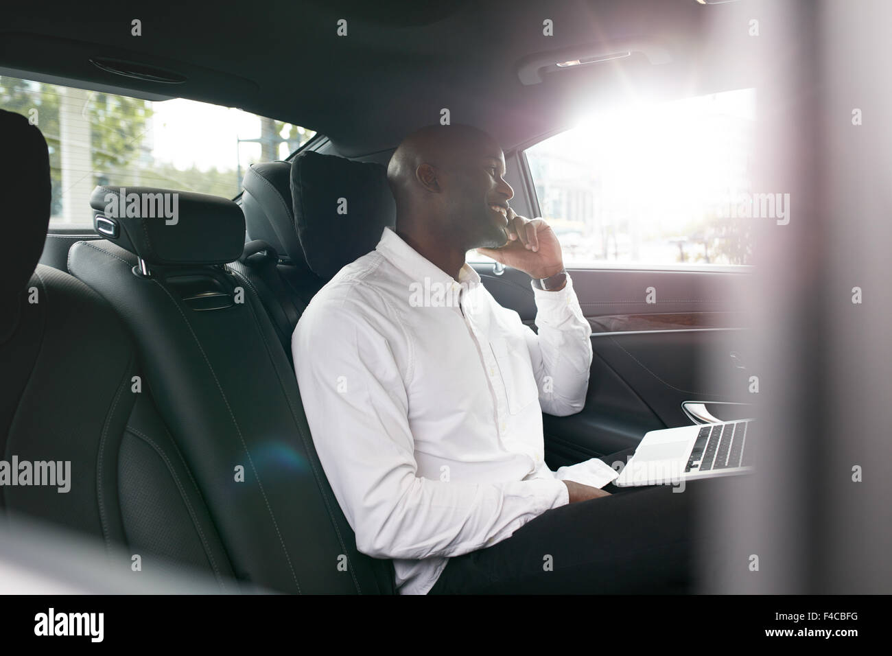 Afrikanischen Geschäftsmann mit Laptop telefonieren mit Handy in einem Auto. Junge Unternehmer arbeiten während der Fahrt zum Büro in Stockfoto