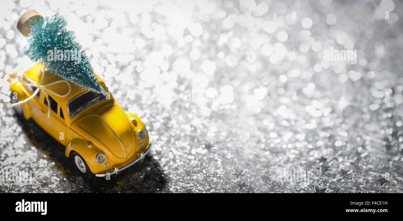 Miniatur gelbes Auto mit Tanne auf silbernem Hintergrund Stockfoto