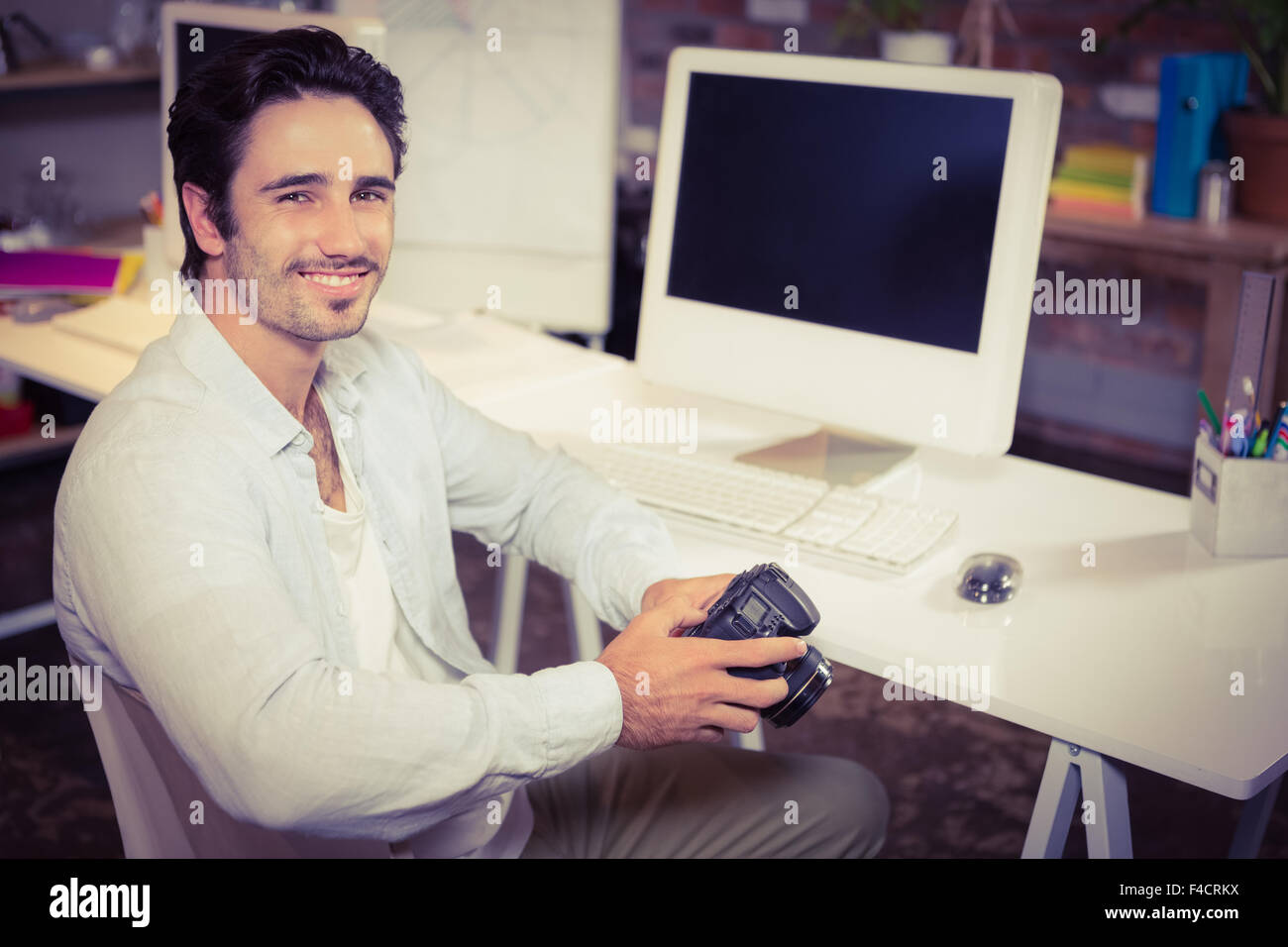 Lächelnder Mann, die Kamera zu halten, am Schreibtisch Stockfoto