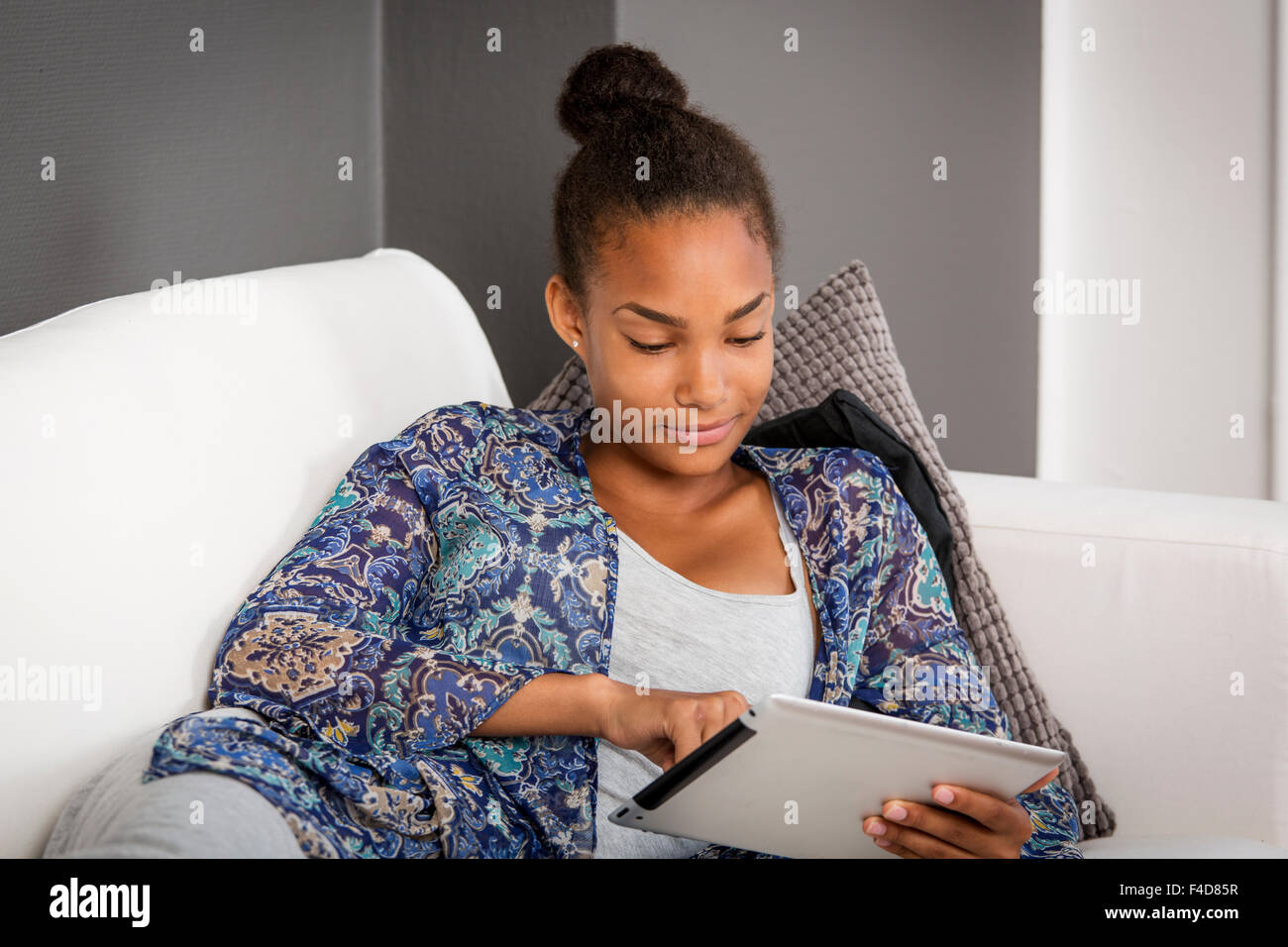 Mädchen in eine Couch mit einem elektronischen Tablet in den Händen. Stockfoto