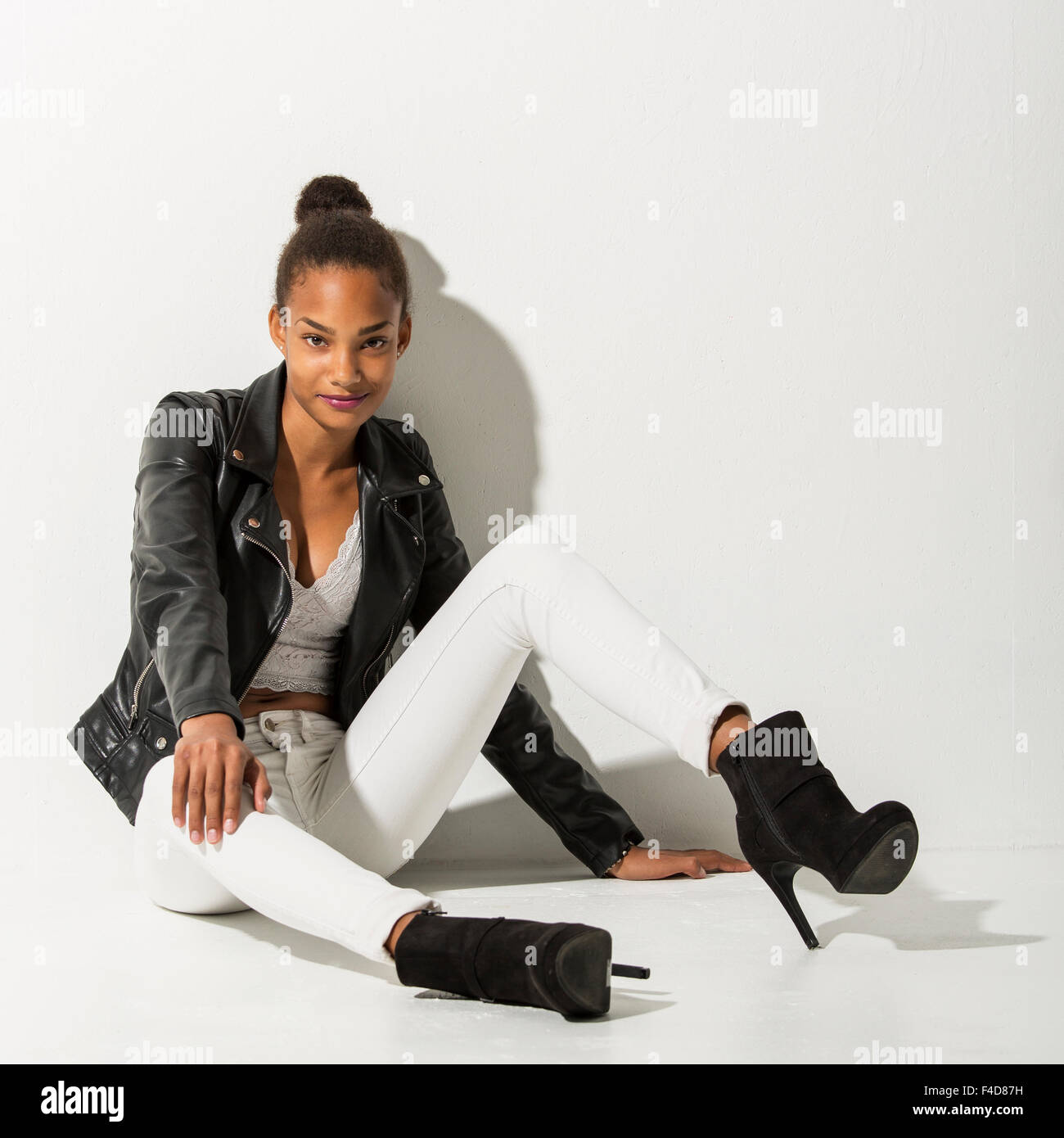 Teenager Mode-Modell sitzt auf einem weißen Boden gegen eine weiße Wand gelehnt. Sie schaut in die Kamera mit einem zuversichtlich smi Stockfoto