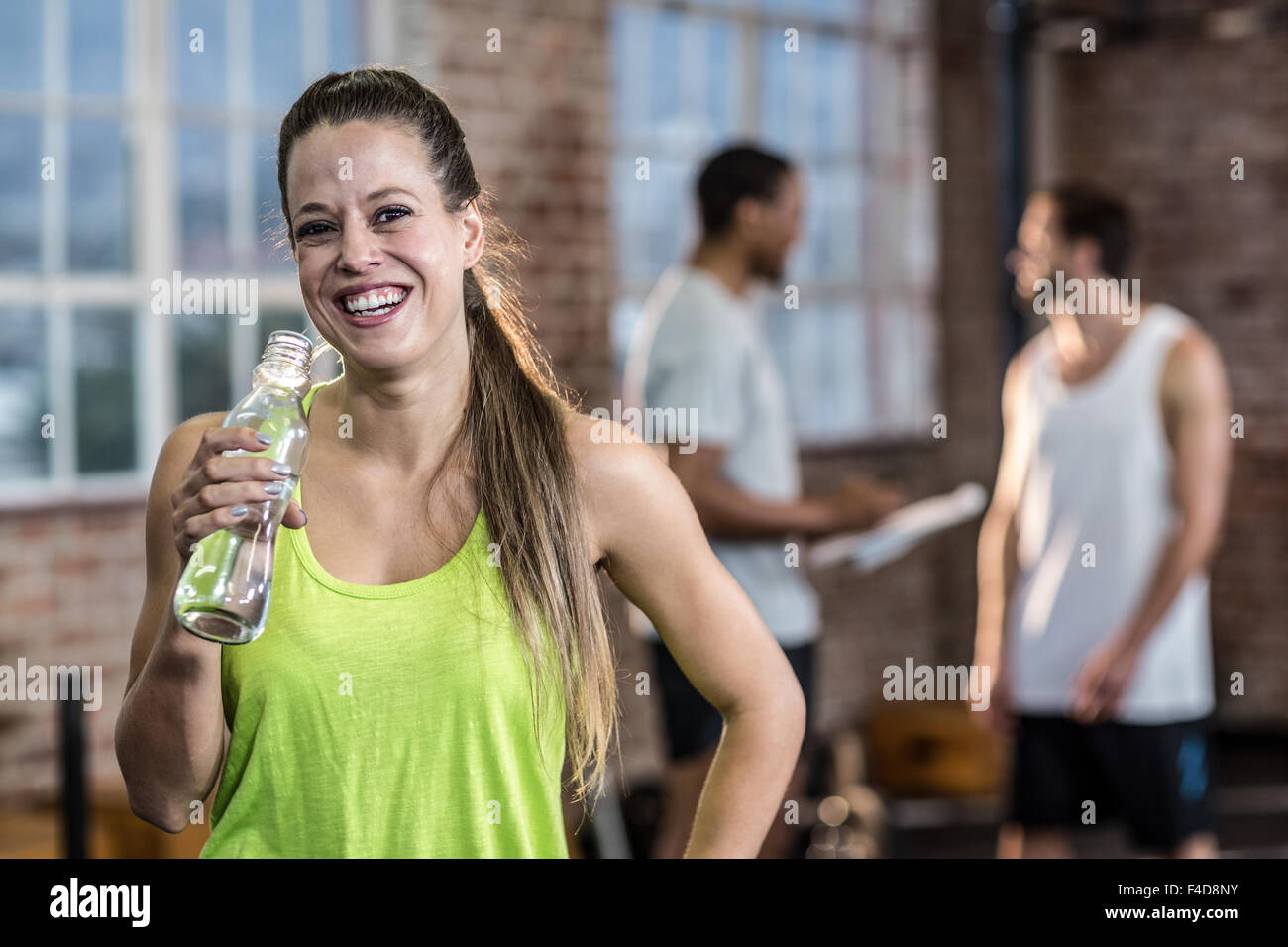 Junge Frau Trinkwasser aus einer Flasche mit Kollegen hinter ihr Stockfoto