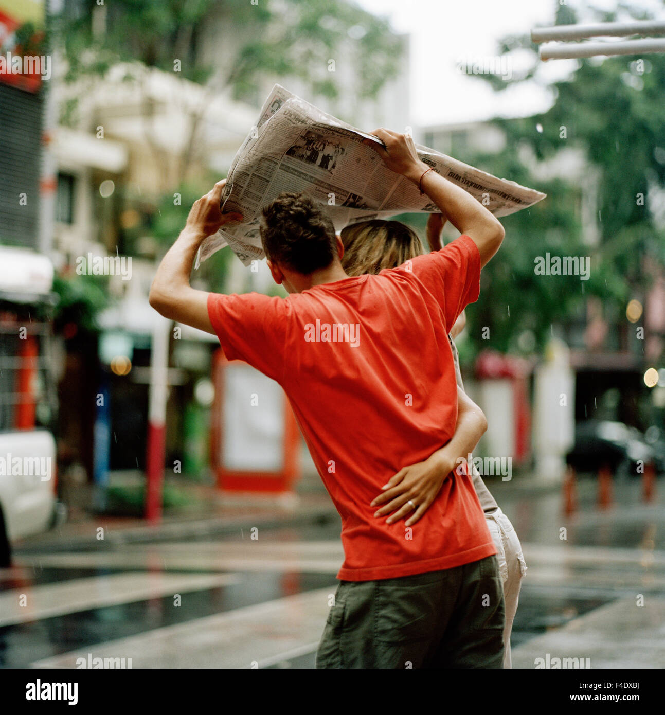 Ein paar mit einer Zeitung als Schutz vor dem Regen, Thailand. Stockfoto