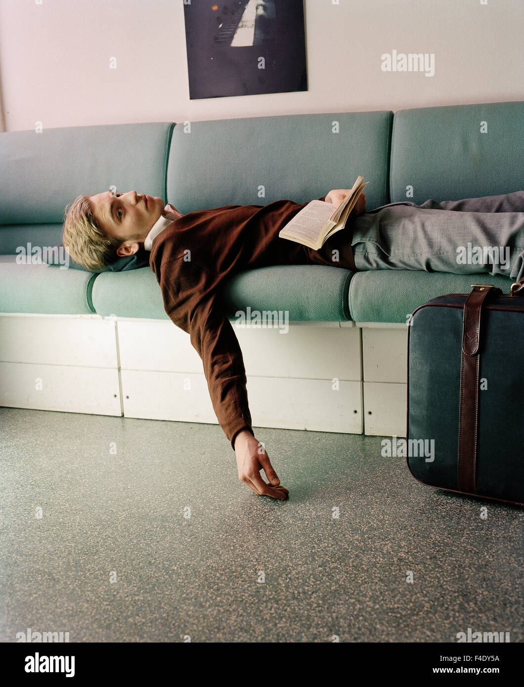 Ein Mann mit einem Buch und einem Koffer Verlegung auf einem Sofa, Schweden. Stockfoto