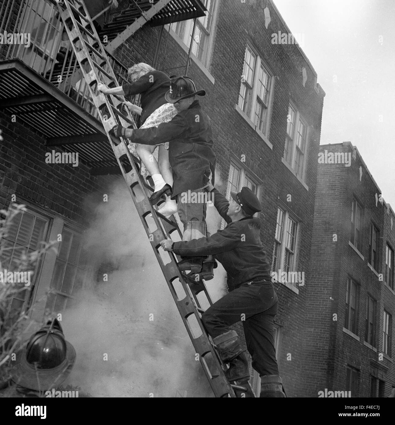 Polizist, Feuerwehrmann Rettungsdienste und ältere Frau bringt ihr unten eine Leiter von einem Rauch gefüllten Wohnung während eines Brandes Stockfoto