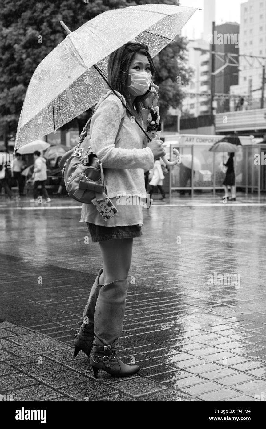 Frau mit Maske und Sonnenschirm steht im Regen zu Beginn des Herbstes in Shibuya, Tokio Stockfoto