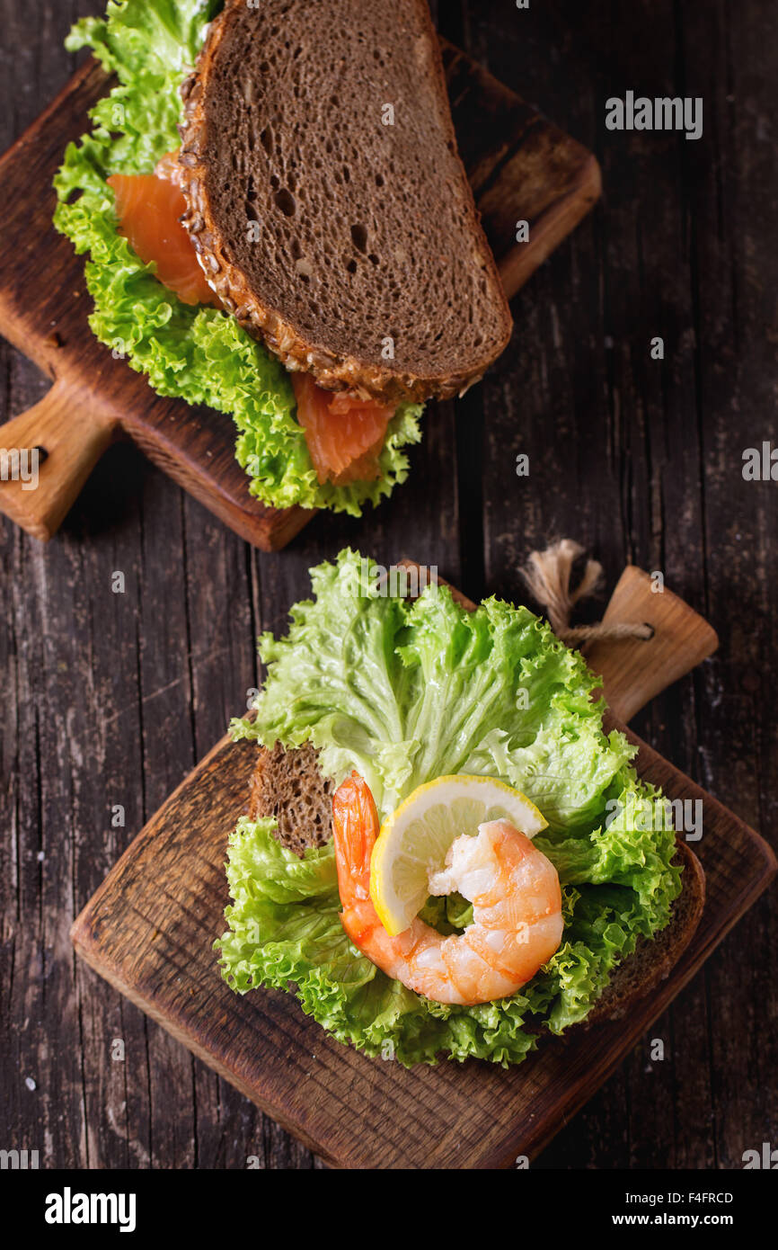 Sandwich mit Vollkornbrot, frischem Salat, Garnelen und gesalzener Lachs auf kleinen Holzbrett über alten Holztisch. Rus Stockfoto