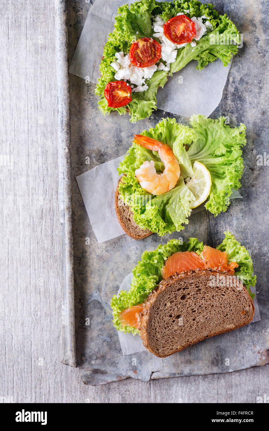 Satz von Sandwiches mit Vollkornbrot, frischem Salat, Feta-Käse, Cherry-Tomaten, Garnelen und gesalzener Lachs auf alte Zinn Hinterg Stockfoto