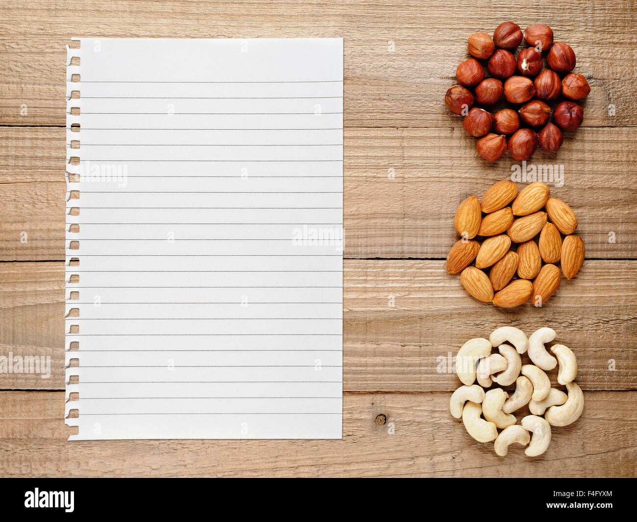 HaselnГјsse, Mandeln, Cashew-Nüssen und Papier für Rezept auf hölzernen Hintergrund Stockfoto