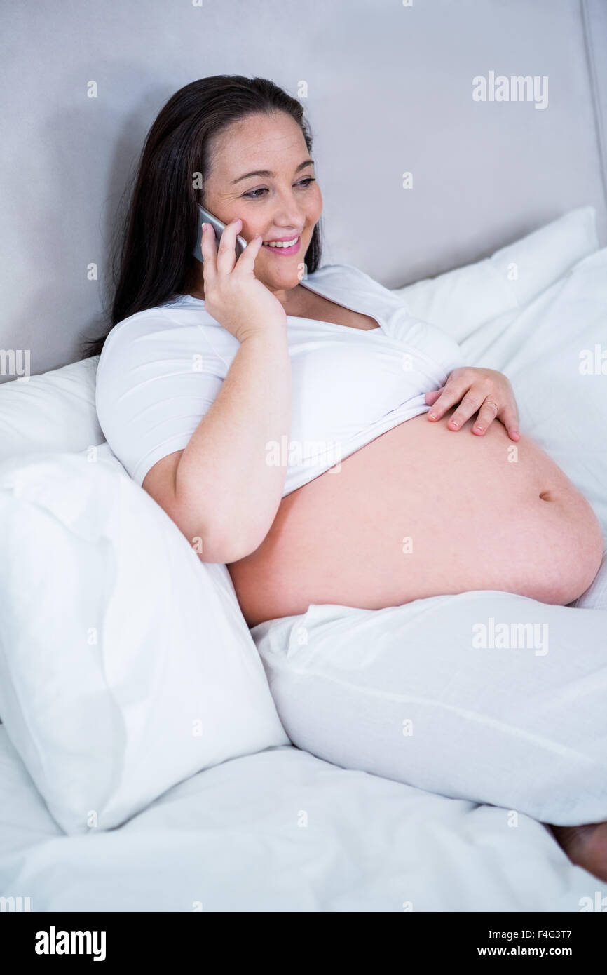 Schwangere Frau auf dem Bett liegend telefonieren Stockfoto