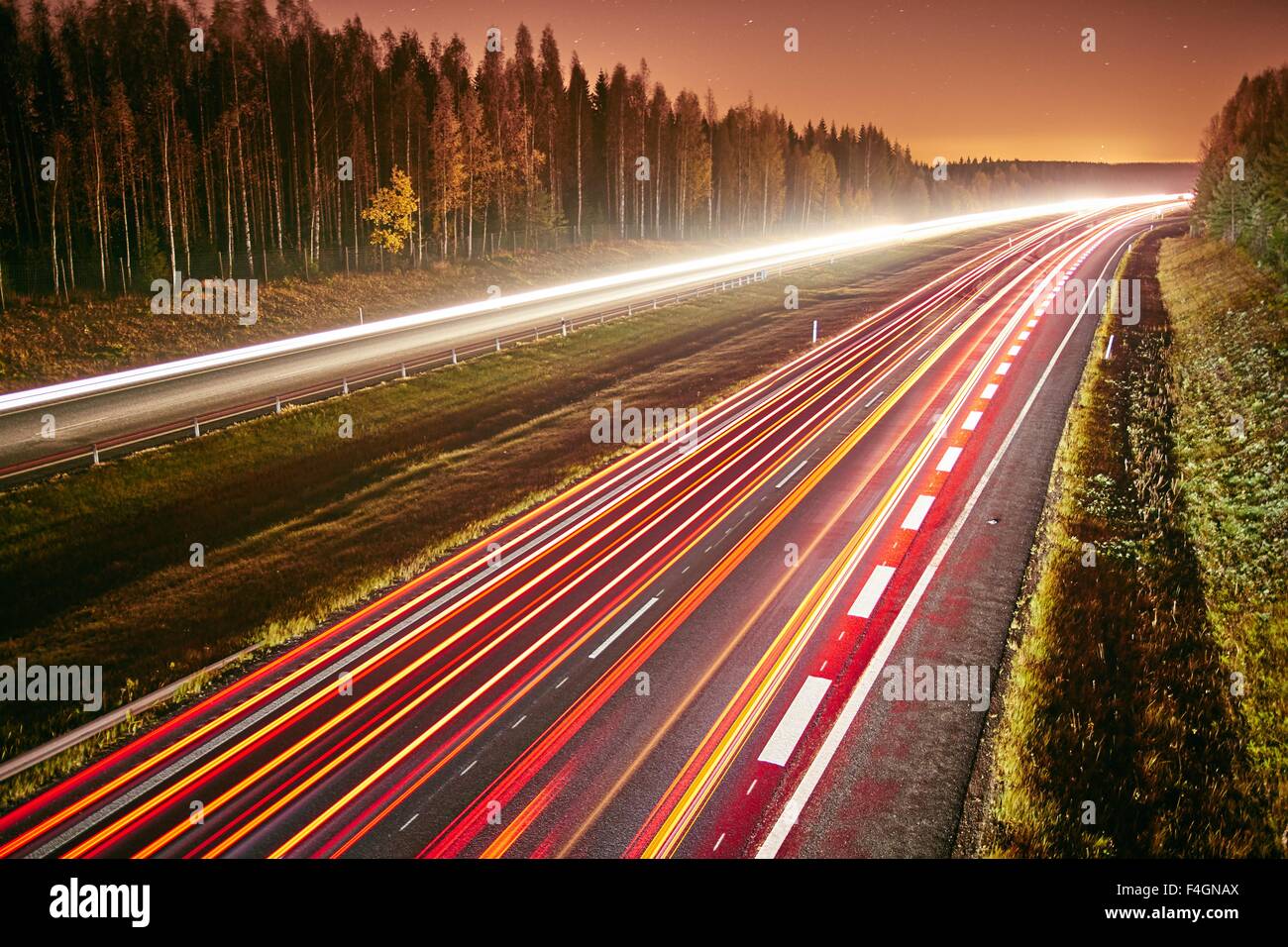 Die Lichtspuren des Autos auf einer Autobahn in der Nacht. Langzeitbelichtung des schnell fließenden Verkehrs in einer sternenklaren Nacht. Stockfoto