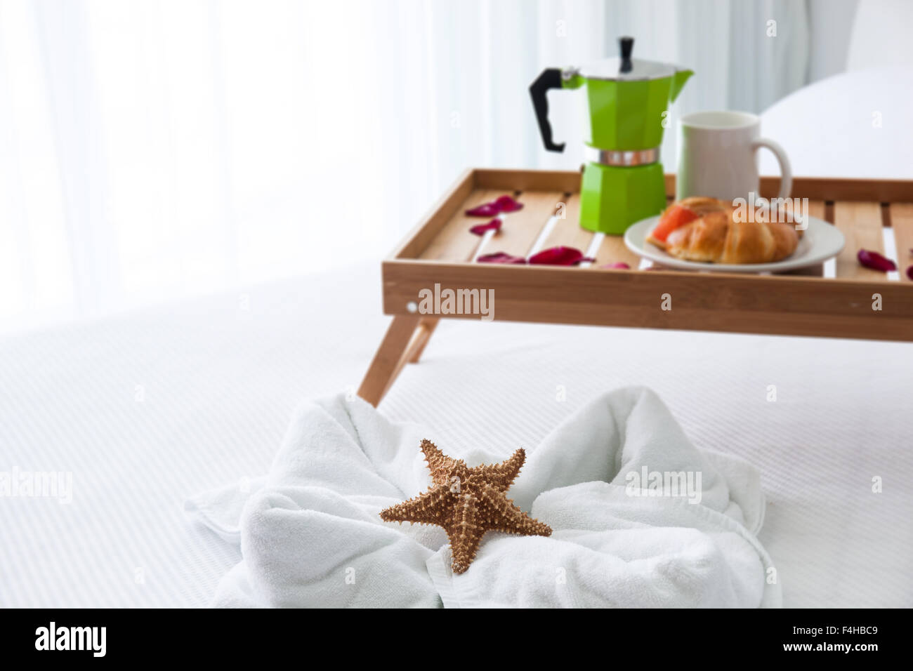 Frühstück Holztablett mit Kaffeemaschine und ein Croissant auf Bett, dekorierte Seestern auf weißen Handtuch Stockfoto