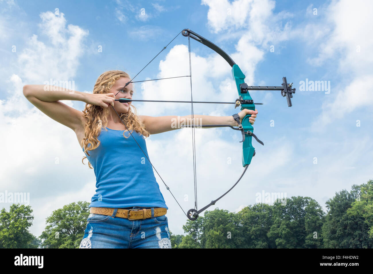 Blonde kaukasische Mädchen schießen mit Pfeil und Verbundbogen im Freien an sonnigen Tag Stockfoto