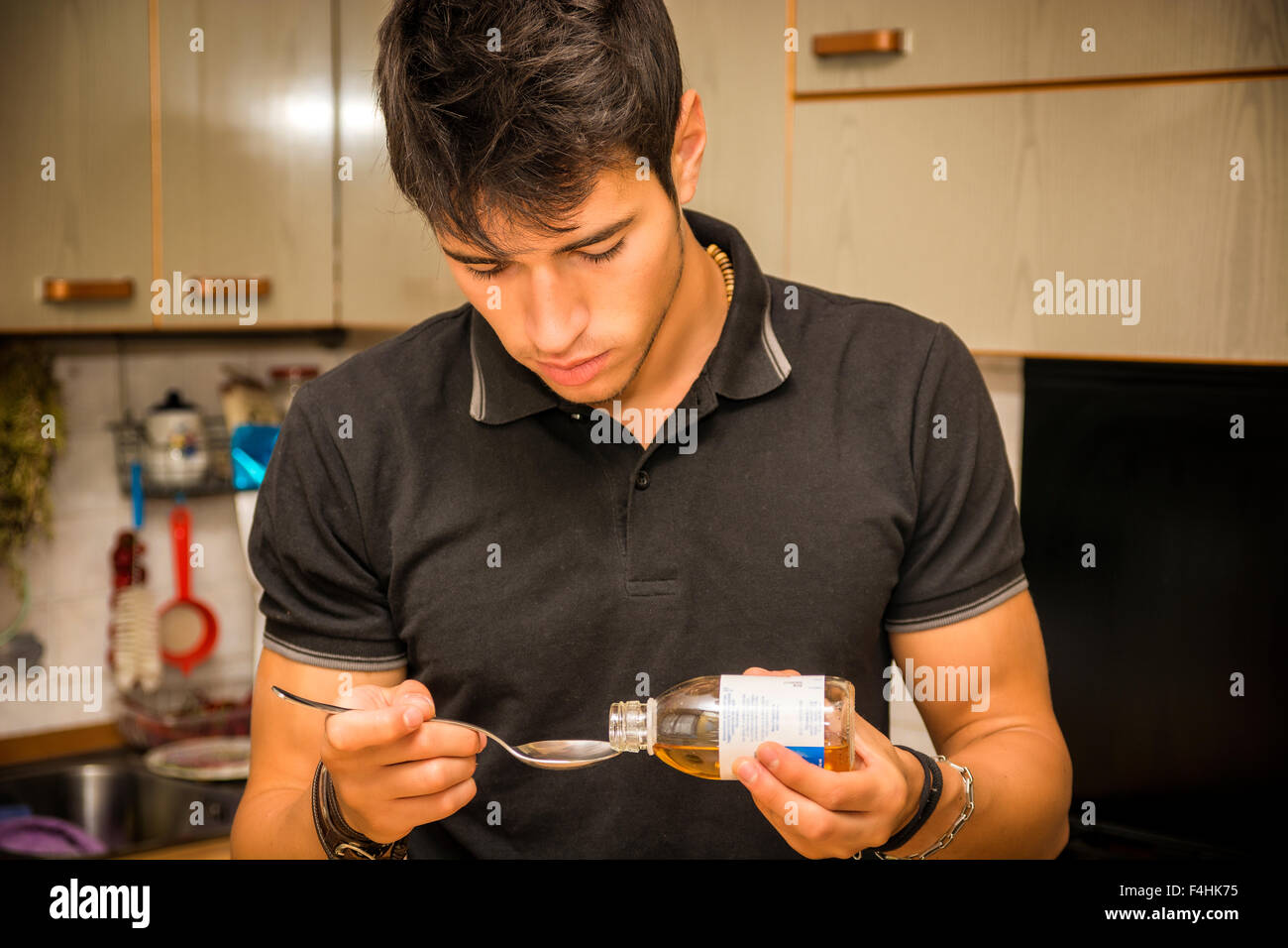 Krank hübscher junger Mann Gießen Hustensaft oder Medikamenten in Löffel, in der Küche zu Hause Stockfoto