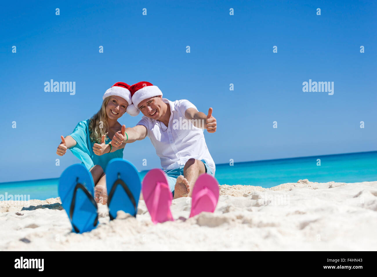Karibik Weihnachten Urlaub am sandigen Strand. Zwei paar Flip flops stehen in einem Sand auf Hintergrund mit emotionalen paar Stockfoto