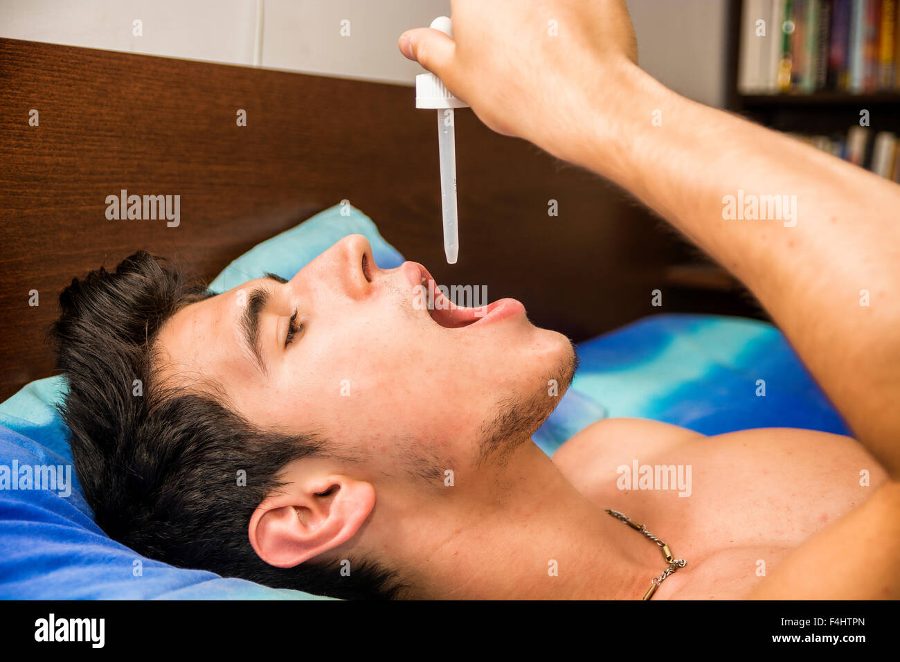 Krank oder unwohl junger Mann mit Pipette Pipette in den Mund für Medizin, medikamentöse Behandlung, beim liegen im Bett Stockfoto