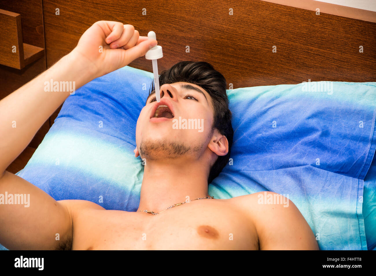 Krank oder unwohl junger Mann mit Pipette Pipette in den Mund für Medizin, medikamentöse Behandlung, beim liegen im Bett Stockfoto