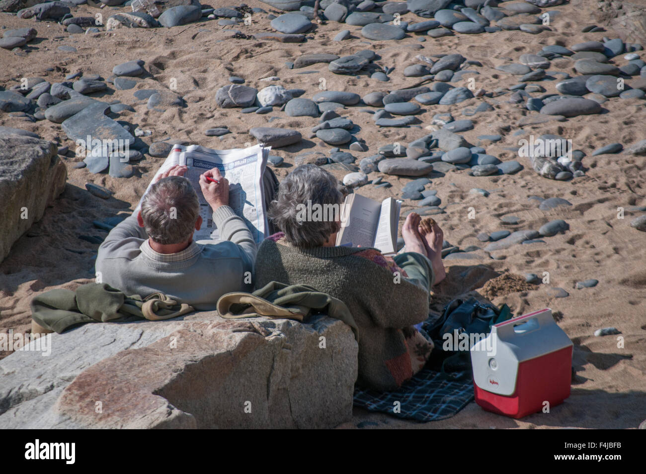 Ein paar in ihren 60 Lesung an einem Strand in Cornwall Stockfoto