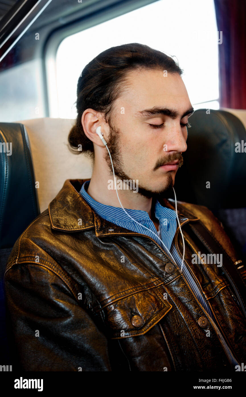 Mann sitzt im Zug mit Augen geschlossen und Musik hören Stockfoto