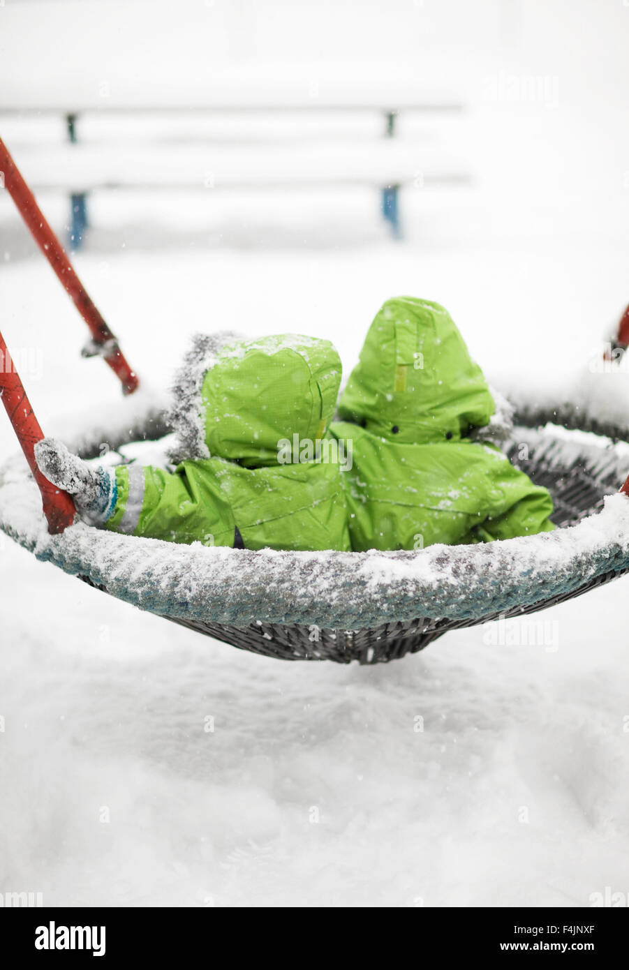 Schweden, Stockholm, paar Kinder Wearig identischen grünen Wintermäntel auf Schaukel mit Schnee bedeckt Stockfoto