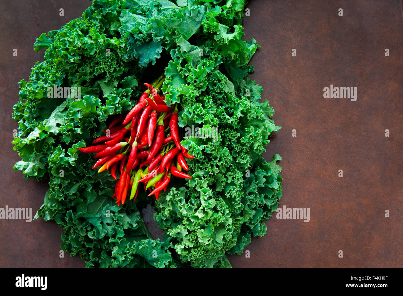 Jede Menge frischen rohen grünen Grünkohl Pflanze und Paprika auf braunen Tisch Stockfoto