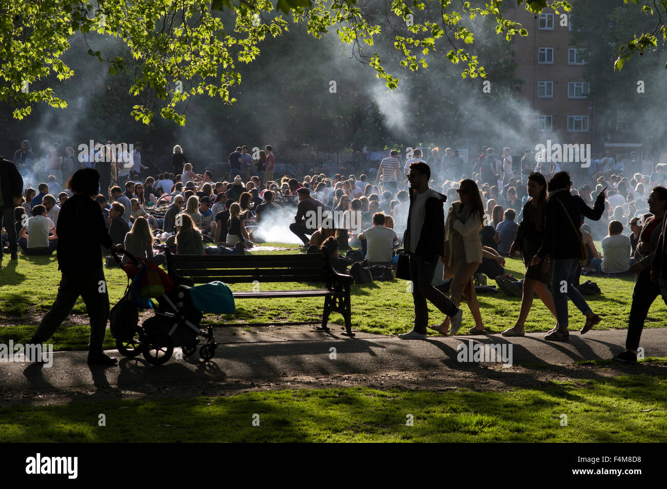 Große Gruppe von Menschen in London Fields Park an einem sonnigen Tag, sitzen auf dem Rasen Grillen, Wolken von Rauch aufsteigt Stockfoto