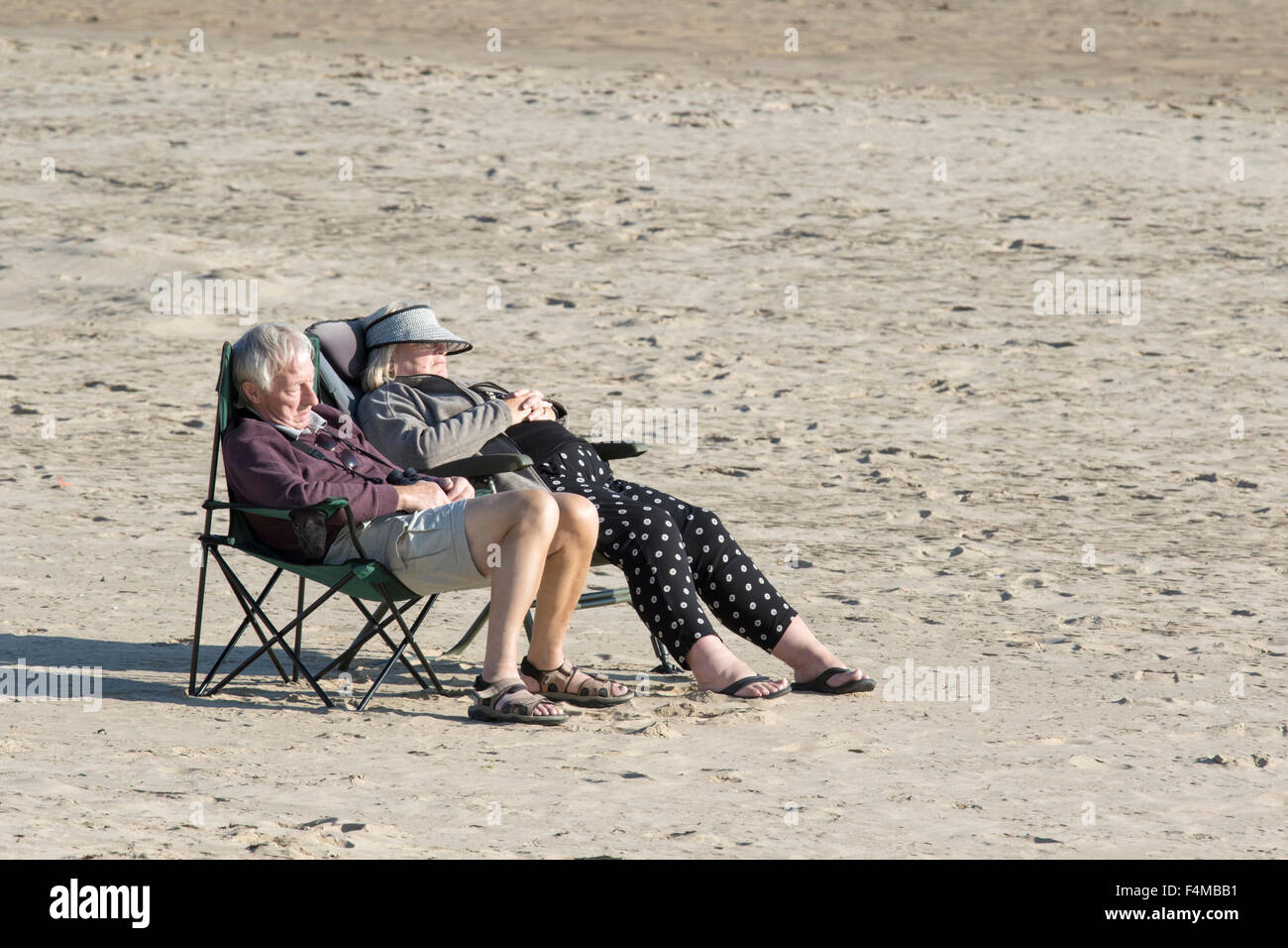 Ein älteres Ehepaar, genießen Sie die Sonne auf einer leeren britischen Strand, England, UK Stockfoto