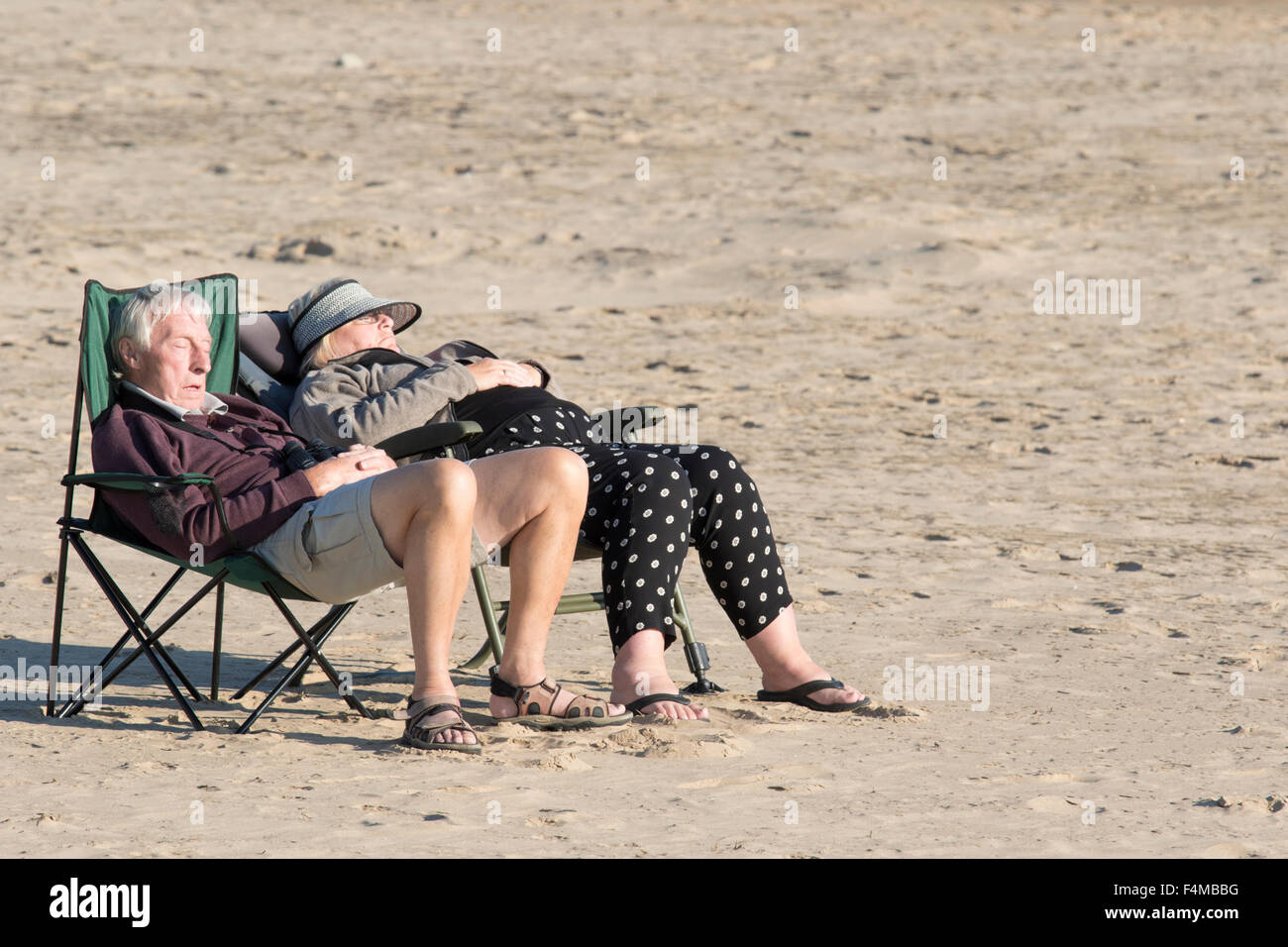 Ein älteres Ehepaar, genießen Sie die Sonne auf einer leeren britischen Strand, England, UK Stockfoto