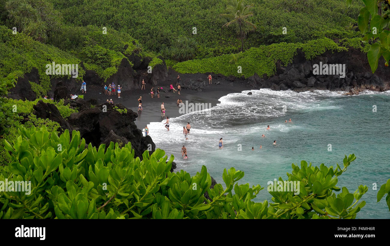 Touristen genießen den schwarzen Sandstrand im Waianapanapa State Park in Maui entlang der Straße nach Hana Stockfoto