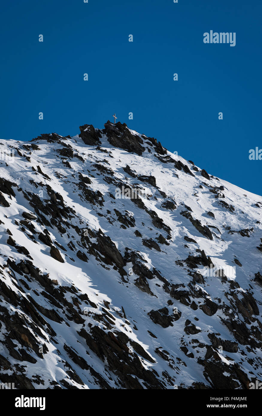 Gipfelkreuz auf einem Schnee bedeckte Berggipfel in den Schweizer Alpen über Belalp, Schweiz (Kanton Wallis). Stockfoto